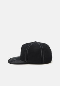 Gorra negra con visera curvada, hecha de una tela suave. Presenta costuras blancas a lo largo de las costuras y un diseño en el lado inferior de la visera.