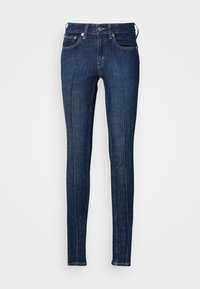 Jeans skinny azul escuro feitos de denim, com uma cintura de altura média, cinco bolsos e costura branca ao longo das costuras.