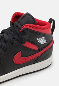Crne kožne tenisice visokog kroja s crvenim akcentima, s podstavom od uzorkovane mrežice, crnim vezicama i bijelim međuslojem. "Air Jordan" logo sa strane.