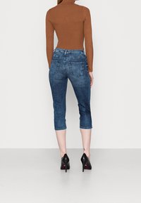 Siniset denim-capri-housut, joissa on tiukka malli, viisi taskua ja hieman kulunut pinta. Yhdistetty mustiin korkeakorkoisiin kenkiin.