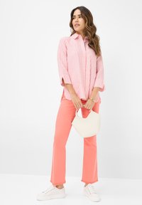 Pink and white striped button-up shirt with rolled sleeves, paired with bright coral pants and a white handbag. White sneakers complete the look.
