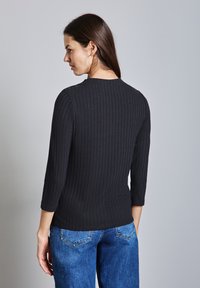 Maglione nero a costine con scollatura tonda e maniche a tre quarti. Abbinato a jeans aderenti a vita alta blu.