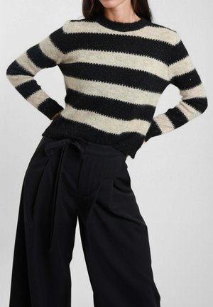 Maglione a righe in crema e nero, realizzato in un materiale tessurizzato con scollatura tonda e maniche lunghe, abbinato a pantaloni neri a vita alta.