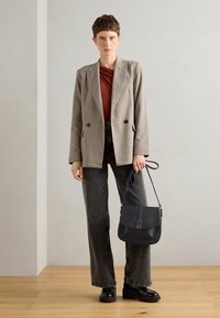 Blazer à motif à carreaux beige et noir, top rouge, jean gris taille haute, chaussures à plateforme noires et sac bandoulière noir avec rabat.
