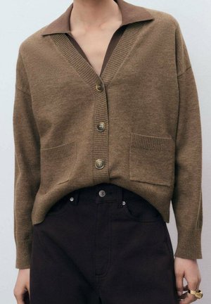 Cardigan en laine marron avec un col contrastant marron foncé, bouton devant, bords côtelés et deux poches avant, associé à un pantalon sombre.