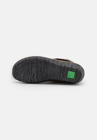 Black rubber sole with wavy texture and branding. Green accent logo embedded in the heel. Sturdy construction suited for outdoor use.