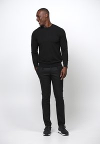 Svart crew-neck tröja, svarta smalbyxor och svarta sportskor. Slät tyg, åtsittande design, minimala detaljer, stående hållning.