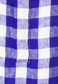 Gros plan d'un tissu à carreaux bleu et blanc avec des coutures visibles et un petit détail de languette rectangulaire.