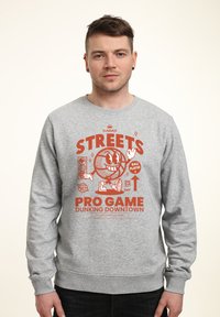 Felpa grigia con una grafica arancione che presenta un pallone da basket cartoon, la scritta "STREETS PRO GAME DUNKING DOWNTOWN" e polsini a costine.