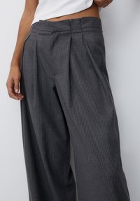 Un pantalon rayé gris avec une taille haute, présentant des plis à l'avant, des jambes larges et une texture lisse. Les rayures sont d'un gris plus clair.