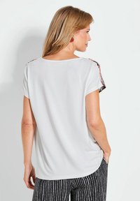 Witte top met korte mouwen en een relaxte pasvorm, met patroonaccenten op de schouders en een gladde textuur. Eenvoudig en veelzijdig ontwerp.