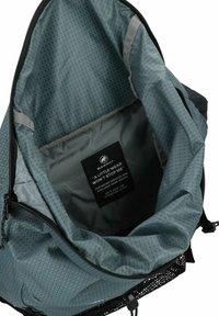 Interieur eines blau-grauen Rucksacks aus strukturiertem Stoff mit geometrischem Muster. Enthält ein Etikett mit Informationen zum Reparaturdienst.