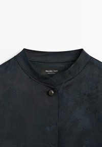 Veste bleu marine à col avec une finition texturée, dotée d'une fermeture à boutons au niveau du cou et d'une étiquette portant la mention "Massimo Dutti".