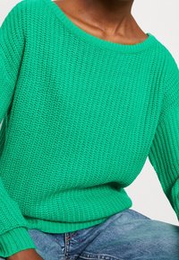 Grön stickad tröja med en lös, avskuren design, ribbade ärmslut och nederkant, med en strukturerad yta.