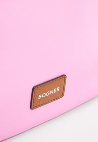 Roza tkanina s površino in rjavim usnjenim obližem z oznako "BOGNER" prišitim nanjo.