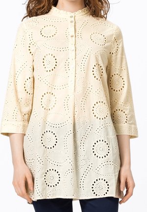 Cream-colored button-up blouse with eyelet floral cutout patterns and 3/4 length sleeves worn by a person.