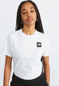 Tricou alb din bumbac cu guler rotund, având un mic patch cu logo negru pe partea stângă și mâneci scurte.