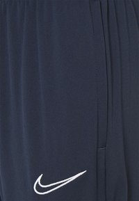 Marina blå Nike sweatpants med elastisk midja, sidofickor och vitt broderat logotyp på vänster lår. Slät tygtextur.