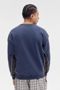 Marineblå hettegenser med kontrasterende svarte sidepaneler og hvite detaljer; har rund hals og ribbestrikkede mansjetter, brukt over rutete shorts.