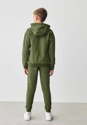 Groene hoodie en sweatpants set van zacht materiaal, met een capuchon met trekkoord en geribbelde boorden, gecombineerd met witte sneakers.