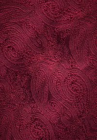 Vinröd textil med ett texturerat mönster av virvlande linjer och upphöjda dekorer, vilket skapar ett rikt och tredimensionellt utseende.