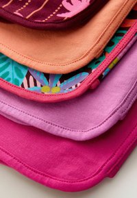 Stakkede stofservietter i forskellige farver: dyb burgunder, fersken, teal, pink og lavendel, med blomster- og geometriske mønstre på nogle kanter.