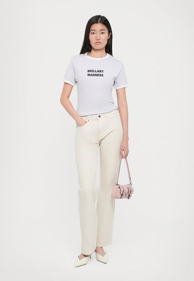 Tricou alb cu text negru "BRILLANT MADNESS", pantaloni largi crem deschis, geantă roz deschis și pantofi cu toc albi.