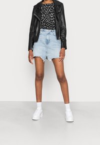 Schwarze Lederbikerjacke, schwarz-weiß gemustertes Oberteil, hellblaue Jeansröcke mit fransigem Saum und weiße Plateausneaker mit weißen Socken.