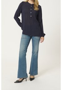 Mörkblå blus med långa ärmar och knäppning framtill, tillsammans med ljusblå utsvängda jeans. Modellen har på sig svarta spetsiga klackskor.