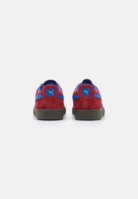 Røde semskede sneakers med blå detaljer, set fra bagsiden som viser den polstrede krave, tekstureret grå ydersål og Puma-logo på hælen og siden.