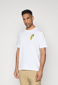 White crew-neck t-shirt with short sleeves, featuring a yellow and green graphic print on the left chest. Soft cotton fabric, relaxed fit.