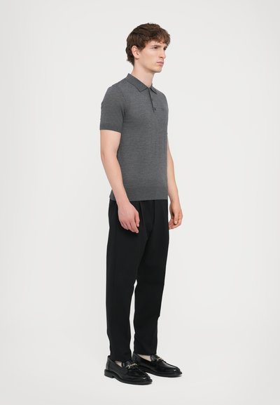 Grå kortærmet polo-shirt med klassisk krave, parret med sorte skræddersyede bukser og sorte sko med metalaccent.