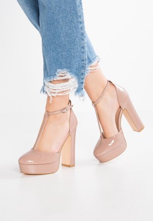 Nude Lackleder High Heels mit T-Riemen, runder Spitze und klobigem Plateau. Mit hochglanzpolierter Oberfläche und Knöchelverschluss.