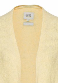 Gerecycled materiaal cardigan in zacht geel, met een V-hals ontwerp en een gestructureerde breiwijze. Binnenlabel toont merk- en maatinformatie.