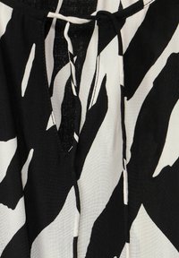 Schwarz-weißer gemusterter Stoff mit einer Mischung aus Streifen und Kurven; verfügt über einen V-Ausschnitt und ein schlankes Bindeband am Hals. Strukturierter Stoff.