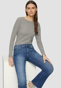 Haut gris à manches longues associé à un jean évasé bleu. La tenue présente une texture lisse, une coupe ajustée et un style décontracté.