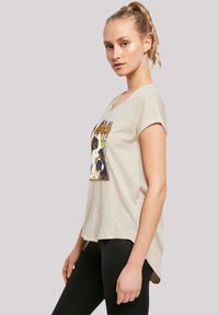 Beige T-Shirt mit kurzen Ärmeln und rundem Ausschnitt, featuring einem grafischen Druck auf der Vorderseite und einem asymmetrischen Saum.
