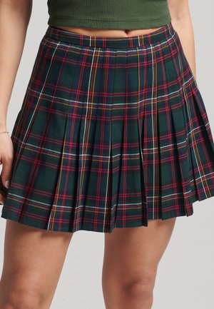 Frau trägt einen kurzen, plissierten Tartan-Rock mit grünem, rotem, weißem und gelbem Karomuster, kombiniert mit einem grünen, kurzen Top.