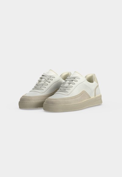 Paire de baskets basses blanches et beige avec lacets sur fond clair uni, vues légèrement en angle.