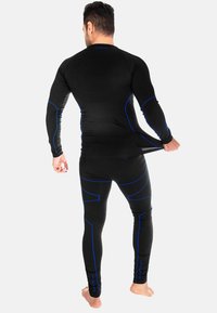 Schwarzes sportliches Langarmoberteil und Leggings mit blauen Akzenten, figurbetontes Design und strukturierter Stoff, von hinten betrachtet.