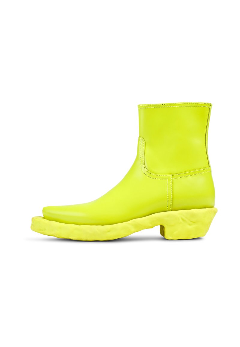Neon gul ankelboot i mjukt läder med en kraftig, texturerad sula som har en unik, oregelbunden form.