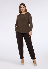 Braunes, glitzerndes Langarmshirt mit Rundhalsausschnitt, seitlichen Taschen und kleinen goldenen Akzenten, kombiniert mit dunkelbraunen, zulaufenden Hose.