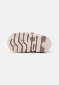 Suela de zapato con un diseño en blanco y púrpura pastel, surcos texturizados, bordes redondeados y agujeros de ventilación con detalles de marca.