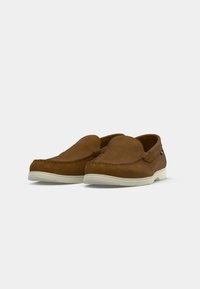 Zapatos de ante marrón estilo mocasín con suela de goma blanca. Presentan costuras a lo largo de los bordes y un pequeño acento decorativo en el lateral.