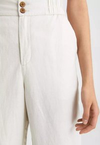 Ljust beige byxor i strukturerad tyg med hög midja, två träknappar och sidofickor.