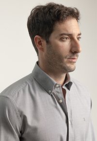 Camisa gris de botones con cuello ajustado, ligero brillo, textura sutil y lema de la marca cerca de los botones.
