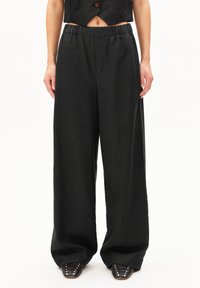 Breda byxor i mörkgrått tyg, med ett elastiskt midjeband för komfort. Slät textur utan synliga mönster; i kombination med spetsiga skor.