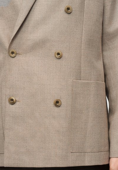 Μπεζ διπλό κουμπωτό σακάκι με τέσσερα καφέ κουμπιά, υφή υφάσματος και μια τσέπη με επένδυση στην αριστερή πλευρά.