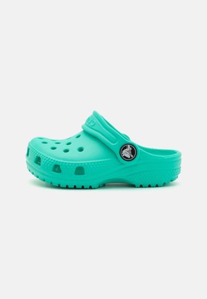 Grønblå slip-on træsko med ventilationshuller, struktureret sål og justerbar hælrem med rund logoemblem.