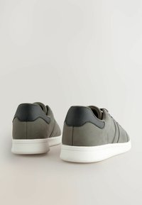 Grey suede sneakers with black leather accents, featuring a white rubber sole and subtle side stripes. Rear view shows clean, minimalist design.